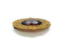 Antique Art Nouveau sash pin brooch crafted from embossed gold-tone brass with swirling whiplash foliage curves, featuring a large prong-set oval faceted purple amethyst glass gemstone center.