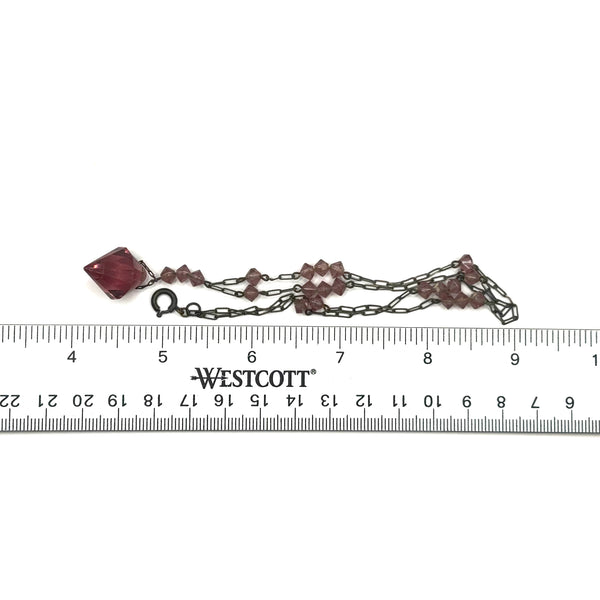 A vintage necklace featuring clusters of deep purple bicone crystal beads on a dark-toned paperclip chain, culminating in a large, heavily faceted diamond-shaped purple crystal drop pendant