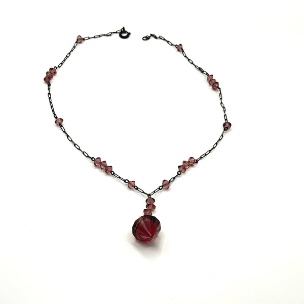 A vintage necklace featuring clusters of deep purple bicone crystal beads on a dark-toned paperclip chain, culminating in a large, heavily faceted diamond-shaped purple crystal drop pendant