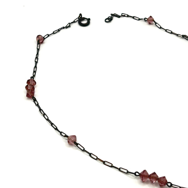 A vintage necklace featuring clusters of deep purple bicone crystal beads on a dark-toned paperclip chain, culminating in a large, heavily faceted diamond-shaped purple crystal drop pendant