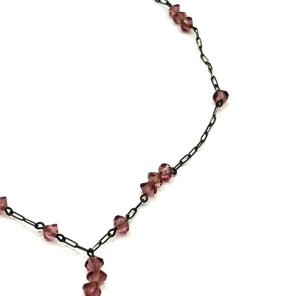 A vintage necklace featuring clusters of deep purple bicone crystal beads on a dark-toned paperclip chain, culminating in a large, heavily faceted diamond-shaped purple crystal drop pendant