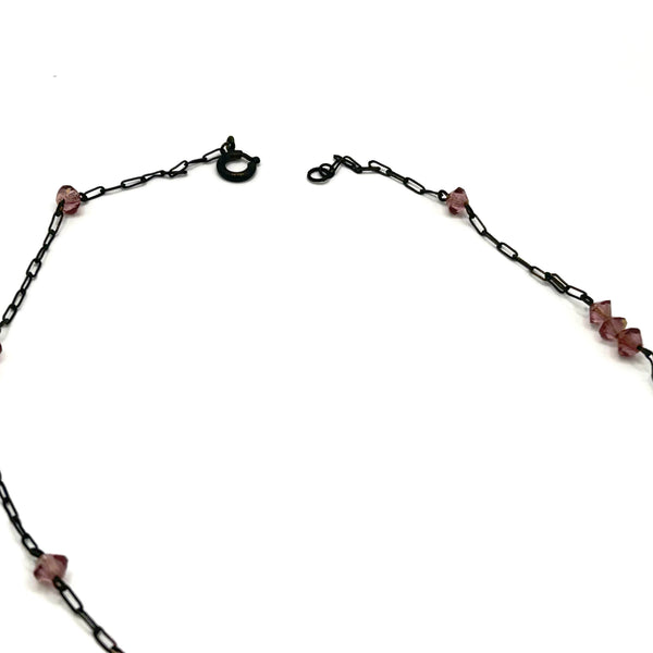 A vintage necklace featuring clusters of deep purple bicone crystal beads on a dark-toned paperclip chain, culminating in a large, heavily faceted diamond-shaped purple crystal drop pendant