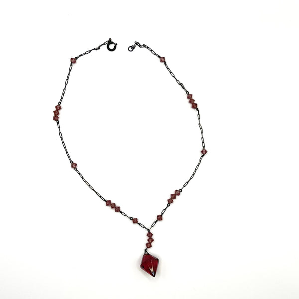 A vintage necklace featuring clusters of deep purple bicone crystal beads on a dark-toned paperclip chain, culminating in a large, heavily faceted diamond-shaped purple crystal drop pendant, displayed on a white jewelry bust