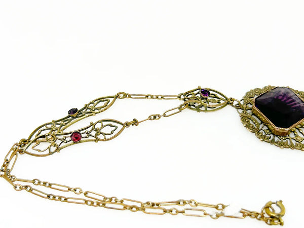 Enhance your jewelry collection with this one-of-a-kind standout piece. Adorned with intricate filigree and glistening purple stones, this necklace exudes elegance and charm. The centerpiece, a stunning diamond-shaped violet stone set in an ornate oval frame, adds a touch of luxury to any outfit