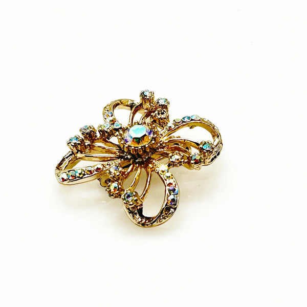 This is a three dimensional vintage ribbon brooch featuring clear rhinestones and a central aurora borealis (AB) gemstone, designed in an abstract floral or bow shape. 