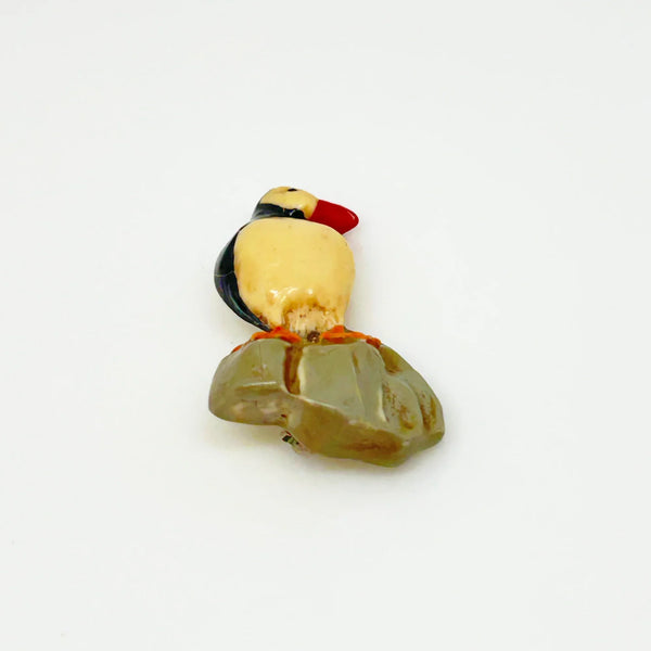This is a brooch by artist Ralph Massey, who is acclaimed for many types of artwork- acrylic, performance, resin and more. This brooch is resin, hand made and hand painted in white, black, red-orange and gray. It depicts a penguin standing on rock, and measures about 1.75” inches tall.