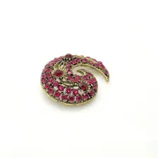 Close-up detail of a mid-century paisley swirl pin showing the openwork metal vines and prong-set pink and red rhinestone crystals