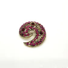 Close-up detail of a mid-century paisley swirl pin showing the openwork metal vines and prong-set pink and red rhinestone crystals