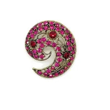 A semi- circular brooch featuring a spiral design filled with pink gemstones and accented by red gemstones on a white background.