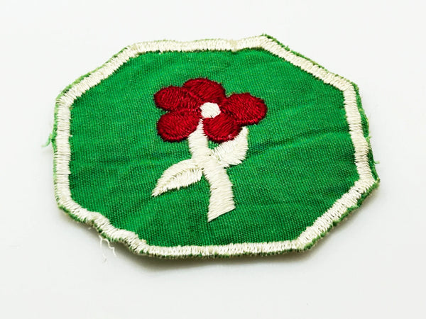 This is a vintage Girl Scout troop crest patch, featuring a red flower design with a white center and stem on a green octagonal background. This specific design has been retired. It depicts either a Scarlet Pimpernel or a Cardinal Flower, with the specific name depending on the era it was produced.