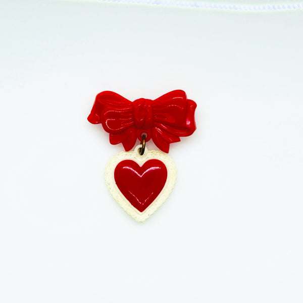 This lovely and nostalgic piece is a vintage early plastic sweetheart bow with dangling filigree lace heart brooch pin, often described as a "Heart Within a Heart" design. It is a recognized "book piece" in vintage jewelry collecting and was commonly made from materials like celluloid plastic .
