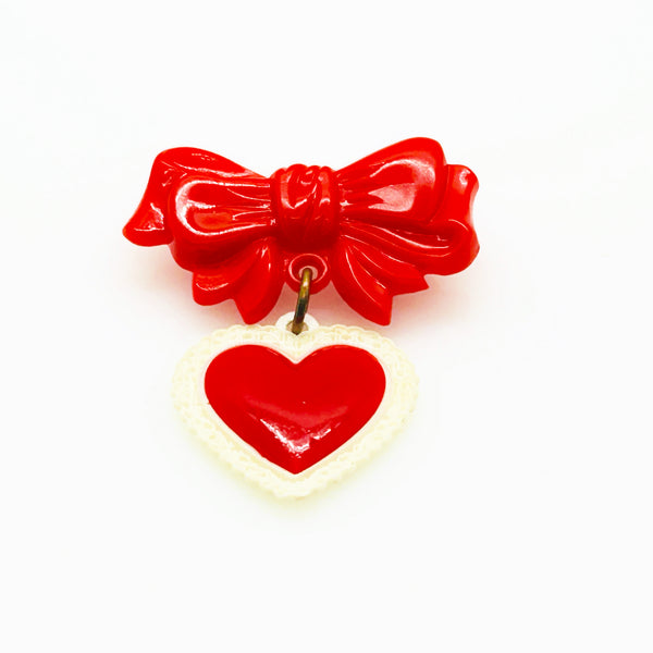 This lovely and nostalgic piece is a vintage early plastic sweetheart bow with dangling filigree lace heart brooch pin, often described as a "Heart Within a Heart" design. It is a recognized "book piece" in vintage jewelry collecting and was commonly made from materials like celluloid plastic .