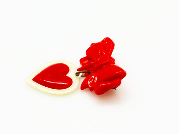 This lovely and nostalgic piece is a vintage early plastic sweetheart bow with dangling filigree lace heart brooch pin, often described as a "Heart Within a Heart" design. It is a recognized "book piece" in vintage jewelry collecting and was commonly made from materials like celluloid plastic .