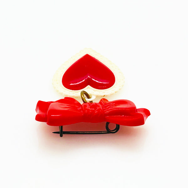 This lovely and nostalgic piece is a vintage early plastic sweetheart bow with dangling filigree lace heart brooch pin, often described as a "Heart Within a Heart" design. It is a recognized "book piece" in vintage jewelry collecting and was commonly made from materials like celluloid plastic .