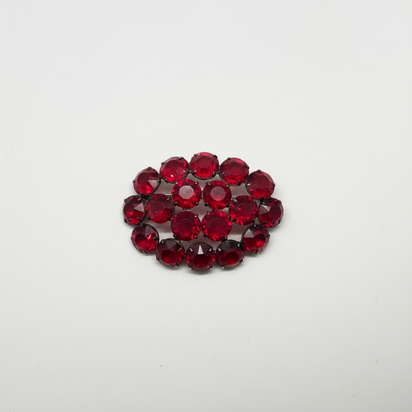 A cluster of faceted round red gemstones arranged in a small oval shape on a plain white background.