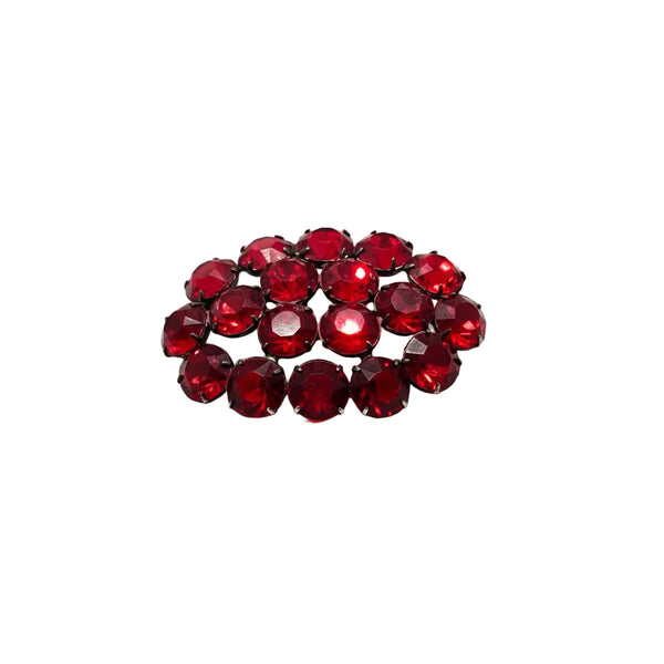 A cluster of faceted deep red rhinestones arranged in a small oval cluster, set in a dark metal prong setting, on a plain white background.