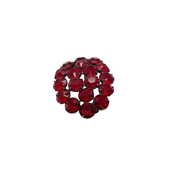 A round cluster of faceted deep red rhinestones set in a dark metal frame, photographed on a plain white background.