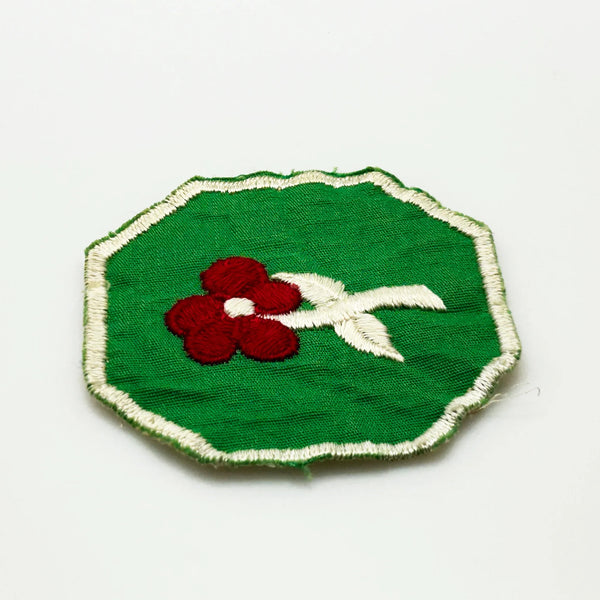 This is a vintage Girl Scout troop crest patch, featuring a red flower design with a white center and stem on a green octagonal background. This specific design has been retired. It depicts either a Scarlet Pimpernel or a Cardinal Flower, with the specific name depending on the era it was produced.