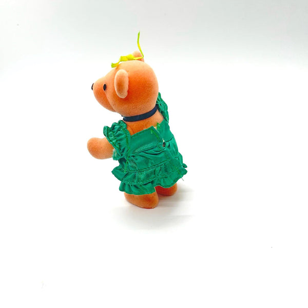 A small plush teddy bear ornament wearing a green floral dress and a yellow bow, standing against a plain white background.
