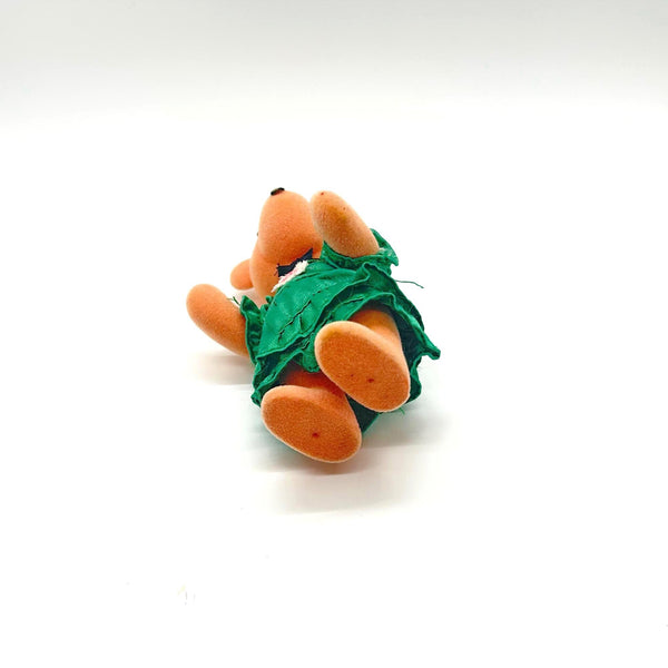 A small plush teddy bear ornament wearing a green floral dress and a yellow bow, standing against a plain white background.