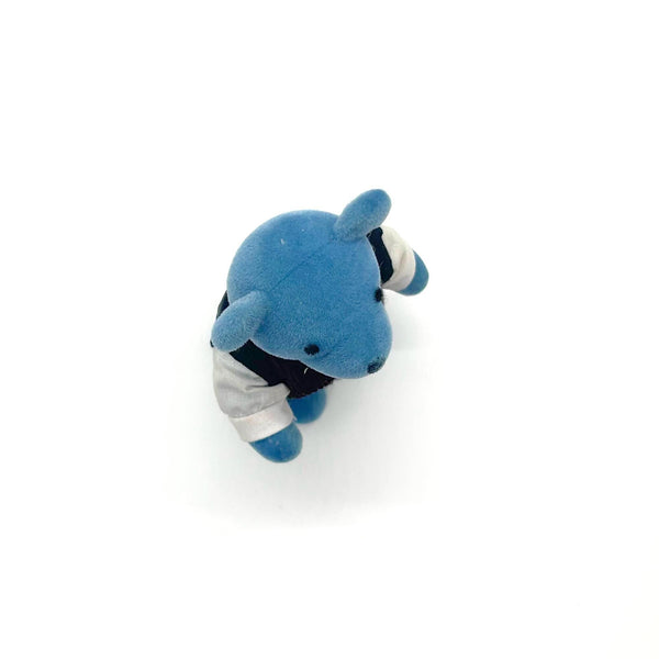 A small blue teddy bear figurine wearing a white shirt, dark vest, striped tie, and dark trousers, standing against a plain white background.