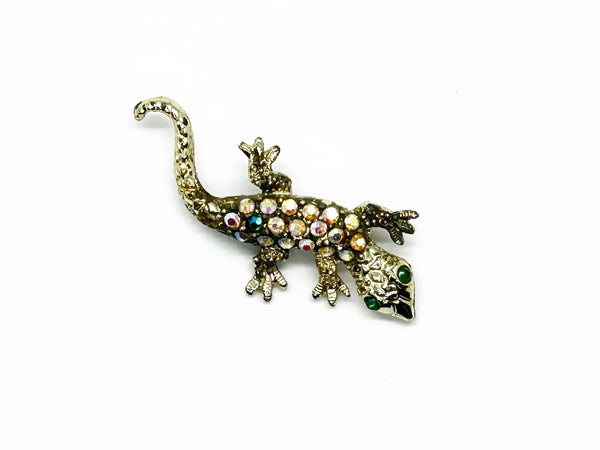This enchanting vintage salamander brooch captures the magic of mid-century costume jewelry with its shimmering Aurora Borealis rhinestones and lustrous gold-toned setting. The iridescent body gleams with multi-colored stones that shift and dance in the light, while striking green accents highlight the creature's expressive eyes.