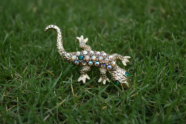 This enchanting vintage salamander brooch captures the magic of mid-century costume jewelry with its shimmering Aurora Borealis rhinestones and lustrous gold-toned setting. The iridescent body gleams with multi-colored stones that shift and dance in the light, while striking green accents highlight the creature's expressive eyes.
