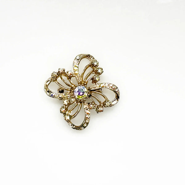 This is a three dimensional vintage ribbon brooch featuring clear rhinestones and a central aurora borealis (AB) gemstone, designed in an abstract floral or bow shape. 