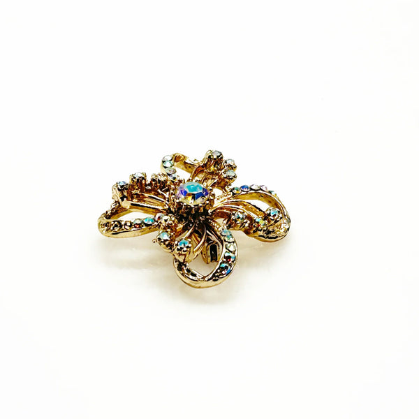 This is a three dimensional vintage ribbon brooch featuring clear rhinestones and a central aurora borealis (AB) gemstone, designed in an abstract floral or bow shape. 
