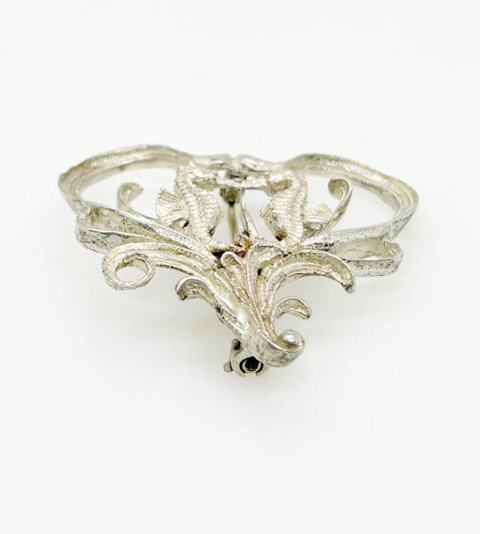 This unusual vintage open work brooch, meeting in a heart shaped frame, is sure to add a unique touch to any ensemble or collection. The detail and flourishes are lovely. The brooch measures 1.75" across at the widest area, and is in very good condition.