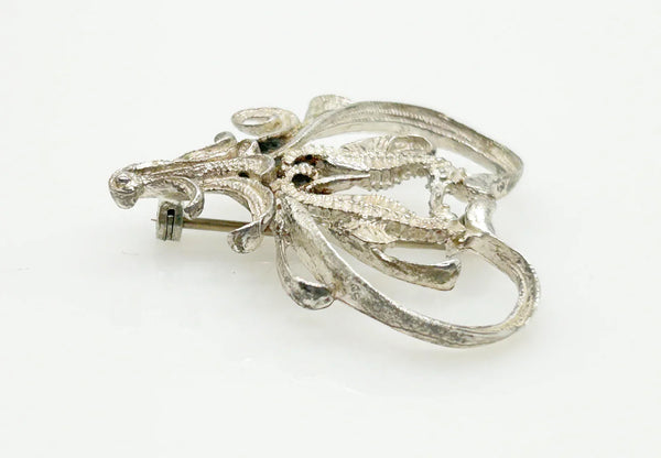 This unusual vintage open work brooch, meeting in a heart shaped frame, is sure to add a unique touch to any ensemble or collection. The detail and flourishes are lovely. The brooch measures 1.75" across at the widest area, and is in very good condition.