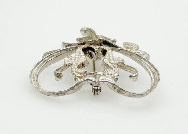 This unusual vintage open work brooch, meeting in a heart shaped frame, is sure to add a unique touch to any ensemble or collection. The detail and flourishes are lovely. The brooch measures 1.75" across at the widest area, and is in very good condition.