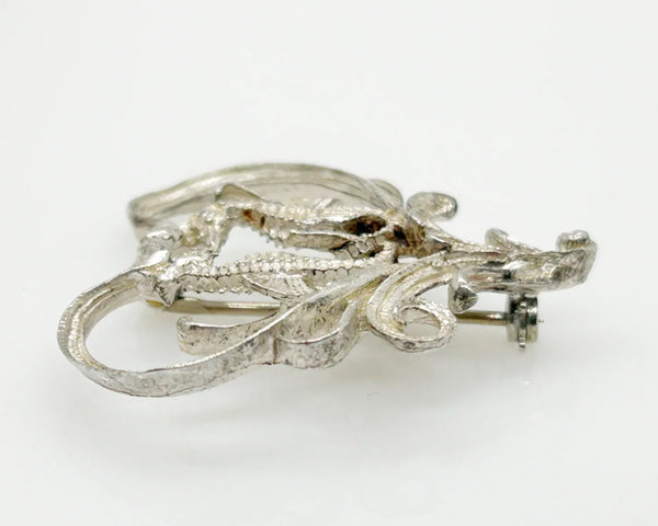 This unusual vintage open work brooch, meeting in a heart shaped frame, is sure to add a unique touch to any ensemble or collection. The detail and flourishes are lovely. The brooch measures 1.75" across at the widest area, and is in very good condition.