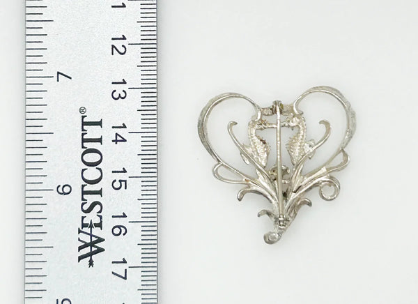 This unusual vintage open work brooch, meeting in a heart shaped frame, is sure to add a unique touch to any ensemble or collection. The detail and flourishes are lovely. The brooch measures 1.75" across at the widest area, and is in very good condition.