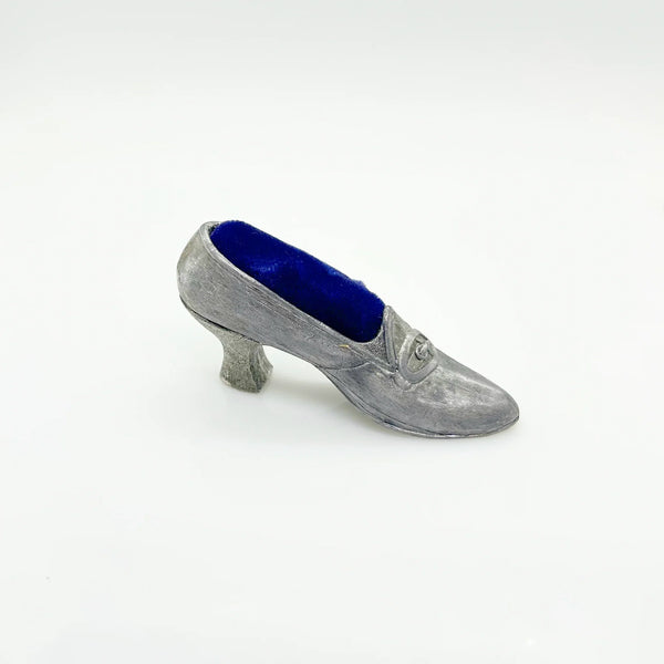 This dainty vintage pincushion is just the thing the add a unique touch to your surroundings. It is made of pewter in the shape of a shoe, with a classic loafer type detail at the toe. It has a .75" kitten heel, and the insole is filled with dark blue, midnight velvet.