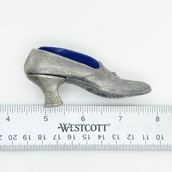 This dainty vintage pincushion is just the thing the add a unique touch to your surroundings. It is made of pewter in the shape of a shoe, with a classic loafer type detail at the toe. It has a .75" kitten heel, and the insole is filled with dark blue, midnight velvet.