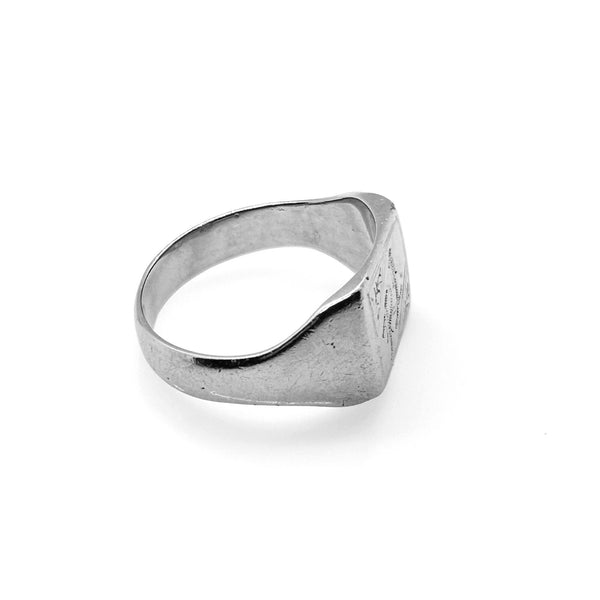 A silver signet ring with a textured, slightly worn finish and engraved lettering on the face, shown on a clean white background.