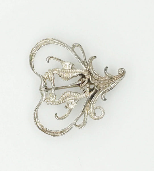 This unusual vintage open work brooch, meeting in a heart shaped frame, is sure to add a unique touch to any ensemble or collection. The detail and flourishes are lovely. The brooch measures 1.75" across at the widest area, and is in very good condition.