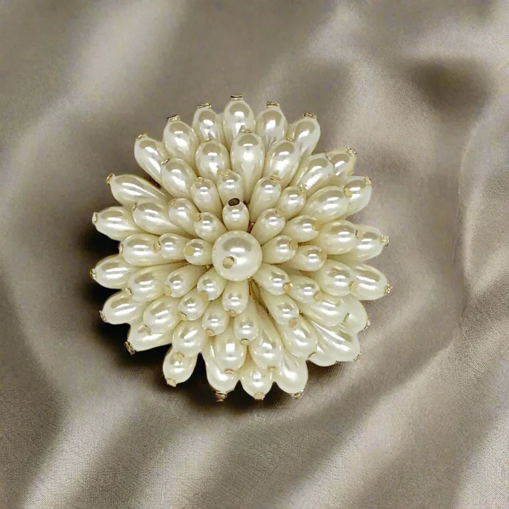 This exquisite flower brooch exudes elegance, featuring stunning faux teardrop pearls set on a captivating gold tone metal frame measuring 2.75” in diameter. It looks like a luxe chrysanthemum. 