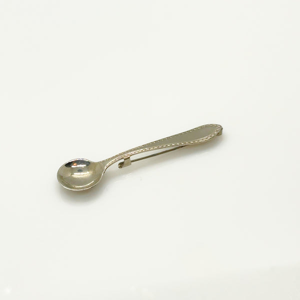 A vintage-style silver-toned metal pin with a spoon-shaped head and a long, narrow pin stem, photographed on a plain white background.
