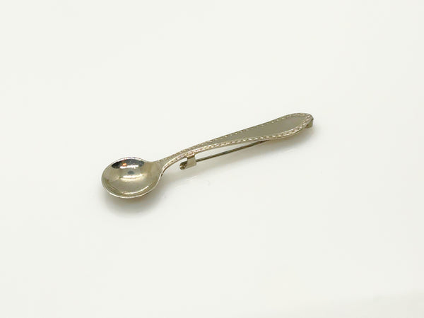 A vintage-style silver-toned metal pin with a spoon-shaped head and a long, narrow pin stem, photographed on a plain white background.