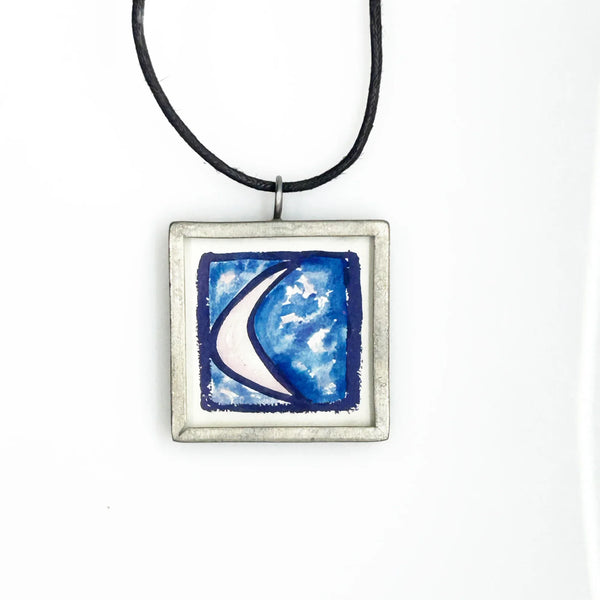 This is a modern inspiration in the form of a square pendant centering around the quote "Every possibility begins with the courage to imagine" by Mary Anne Radmacher. The quote is written in black ink, on a white background, and framed in silver metal. The reverse features a blue night sky background with a quarter moon and star. 