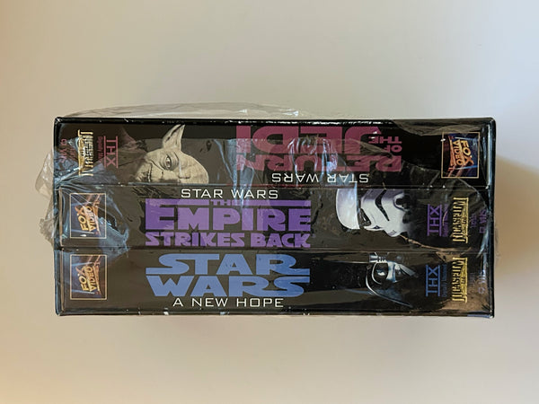 Side view of a vintage 1995 Star Wars Original Trilogy 3-tape VHS box set, factory-sealed in plastic shrink wrap against a neutral light background