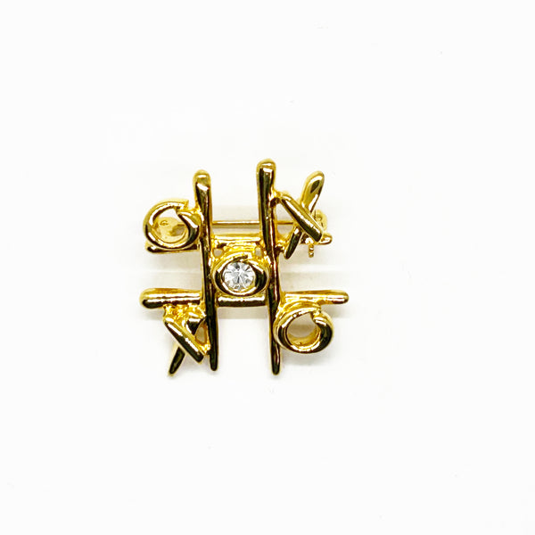 This charming Anne Klein brooch captures the playful spirit of vintage costume jewelry with its clever tic-tac-toe design. Crafted in warm gold tone, the piece features an open-style board complete with X's and O's, crowned by a sparkling clear rhinestone at its center