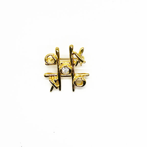 This charming Anne Klein brooch captures the playful spirit of vintage costume jewelry with its clever tic-tac-toe design. Crafted in warm gold tone, the piece features an open-style board complete with X's and O's, crowned by a sparkling clear rhinestone at its center