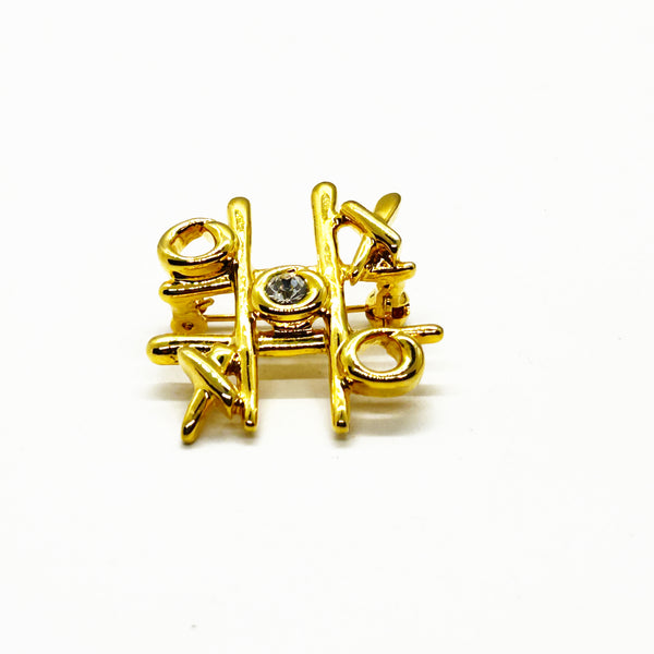 This charming Anne Klein brooch captures the playful spirit of vintage costume jewelry with its clever tic-tac-toe design. Crafted in warm gold tone, the piece features an open-style board complete with X's and O's, crowned by a sparkling clear rhinestone at its center