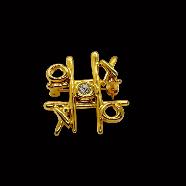 This charming Anne Klein brooch captures the playful spirit of vintage costume jewelry with its clever tic-tac-toe design. Crafted in warm gold tone, the piece features an open-style board complete with X's and O's, crowned by a sparkling clear rhinestone at its center
