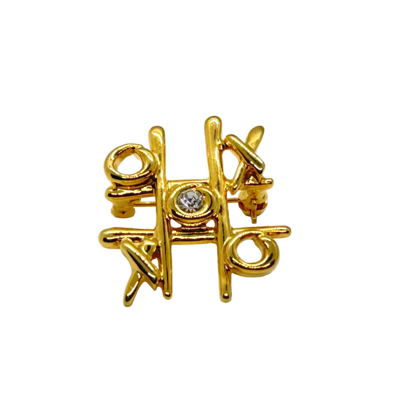 This charming Anne Klein brooch captures the playful spirit of vintage costume jewelry with its clever tic-tac-toe design. Crafted in warm gold tone, the piece features an open-style board complete with X's and O's, crowned by a sparkling clear rhinestone at its center