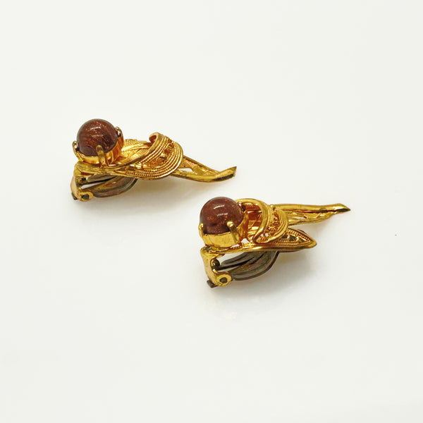 A pair of vintage gold-toned clip-on earrings with round reddish-brown cabochon stones, displayed on a clean white background.