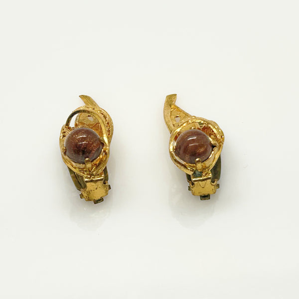 A pair of vintage gold-toned clip-on earrings with round reddish-brown cabochon stones, displayed on a clean white background.